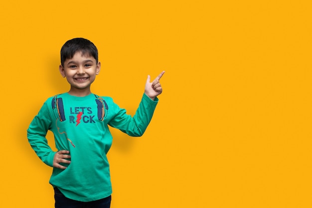 Foto menino feliz em uma camisa apontando para cima e segurando o braço branco olhando para a câmera sobre fundo isolado e espaço de cópia