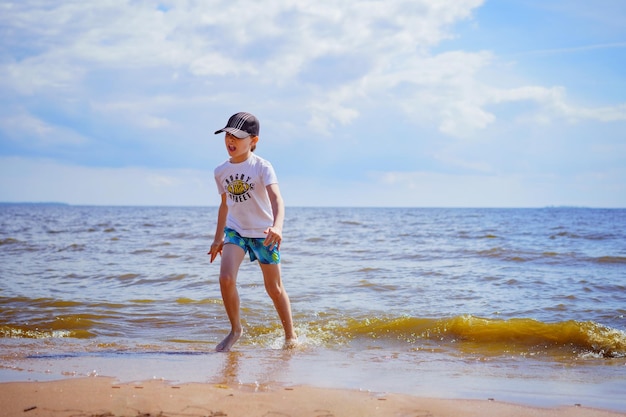 Menino feliz está correndo no mar no dia ensolarado de verão Conceito de infância