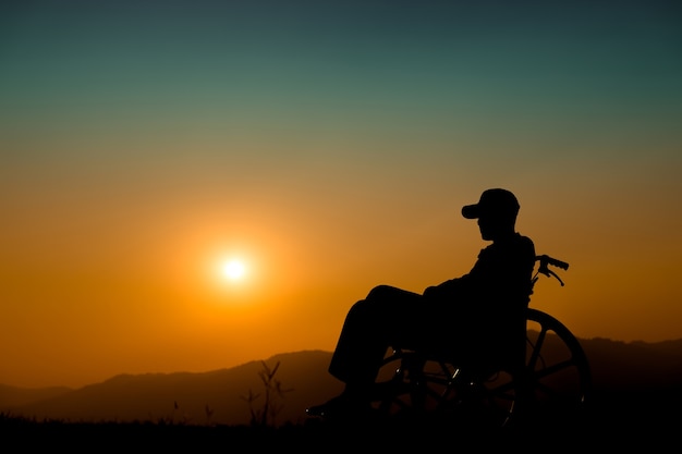 Menino feliz na cadeira de rodas no por do sol Conceito de criança deficiente feliz