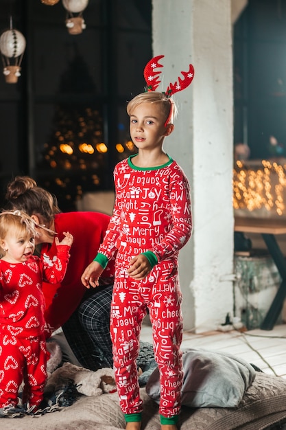 Menino feliz na cama perto, com pijama vermelho de Natal e chifres de veado