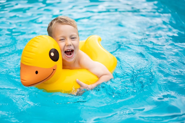 Menino feliz nada na piscina em um círculo inflável de borracha no verão verão fim de semana para crianças crianças de férias no parque aquático