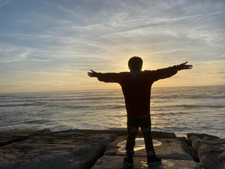 Foto menino feliz olhando para o pôr-do-sol ao lado do mar silhueta de um menino sonhador olhando esperançoso para o horizonte