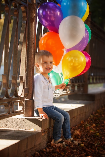 Menino feliz pequeno com os balões coloridos ao ar livre no verão.