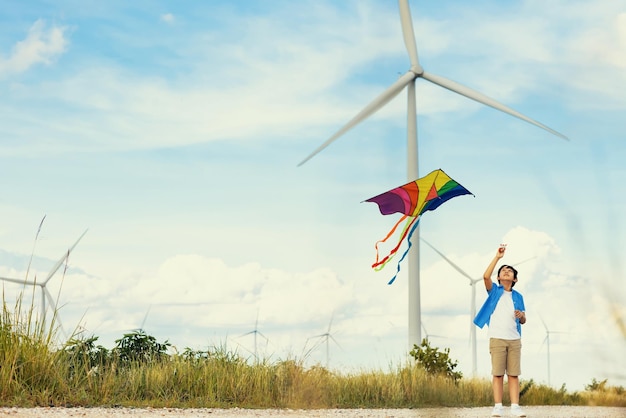 Menino feliz progressivo correndo e empinando pipa com fundo de turbina eólica