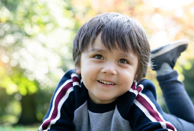 Menino feliz que estabelece na grama no parque com fundo desfocado