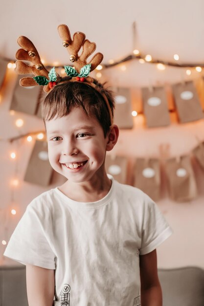 Menino feliz saúda o Natal Clima de Natal em casa Menino se alegra no Natal Manhã de Natal Um menino com chifres de veado saúda o Natal