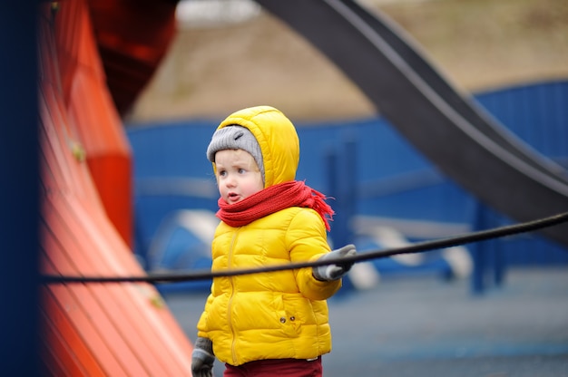 Menino feliz se divertindo no playground ao ar livre. Primavera e outono lazer ativo para as crianças.