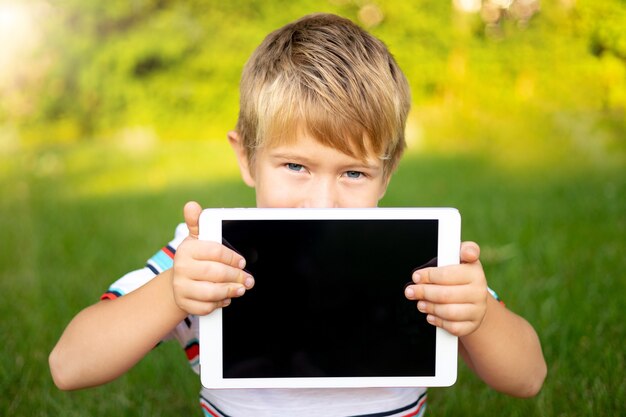 Menino feliz segurando um computador tablet ao ar livre em um parque de verão