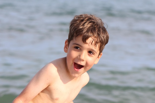 Menino feliz sem camisa gritando enquanto está de pé contra o mar