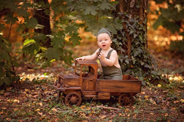 Menino feliz sentado em um carrinho de brinquedo de madeira ao ar livre no verão