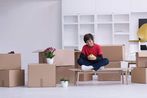 menino feliz sentado na mesa com caixas de papelão ao seu redor em uma nova casa moderna