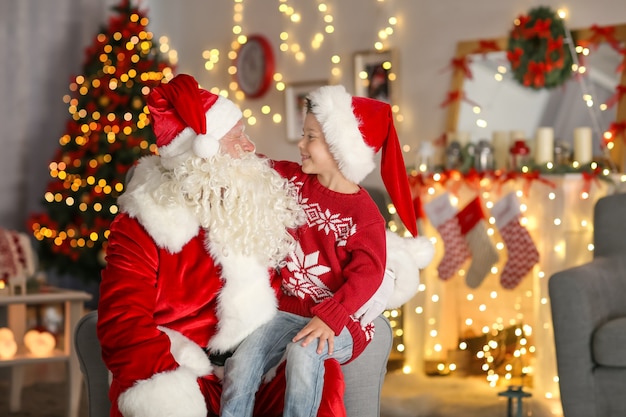 Menino feliz sentado no colo do Papai Noel em uma sala com lindas decorações de Natal