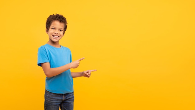 Foto menino feliz sorrindo e apontando para o lado no espaço livre em fundo amarelo