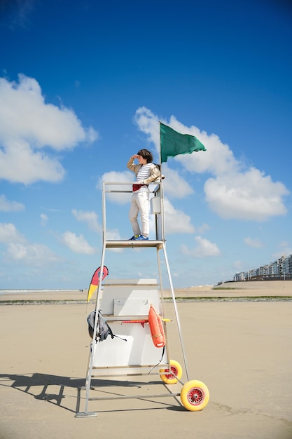 Menino fica na torre de resgate olhando para longe no mar criança brincando de salva-vidas no mar do norte na holanda