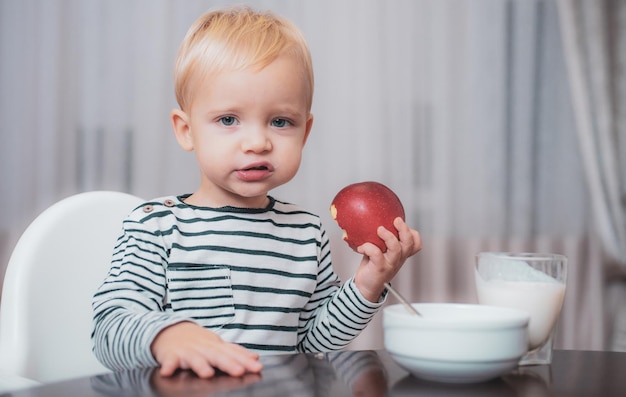 Menino fofo bebê tomando café da manhã nutrição do bebê coma saudável criança fazendo lanche nutrição saudável conceito de vitamina criança come maçã garoto fofo menino sentado à mesa com prato e comida comida saudável