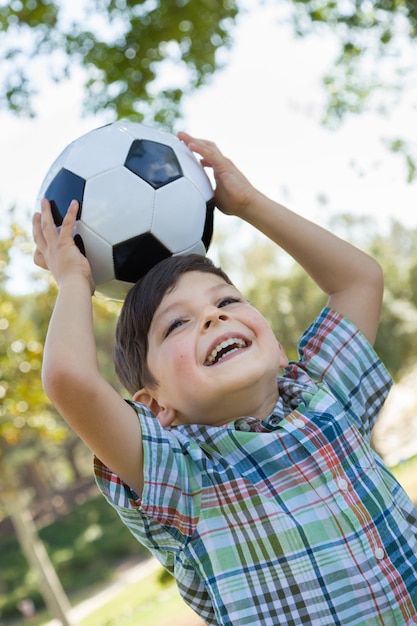 Menino fofo brincando com bola de futebol ao ar livre no parque