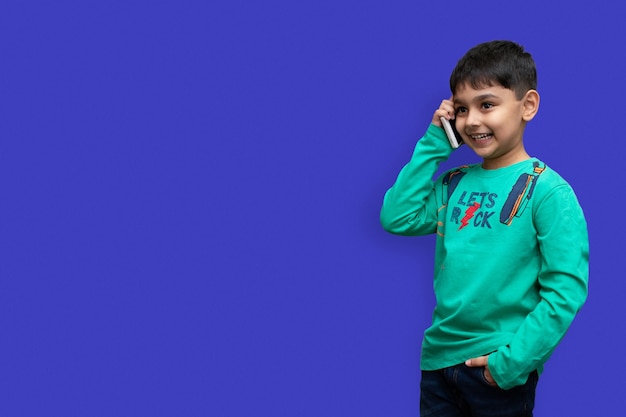 Menino fofo com uma camisa verde falando ao telefone em um fundo simples com espaço de cópia