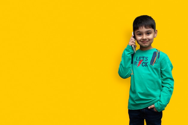 Foto menino fofo com uma camisa verde falando ao telefone em um fundo simples com espaço de cópia