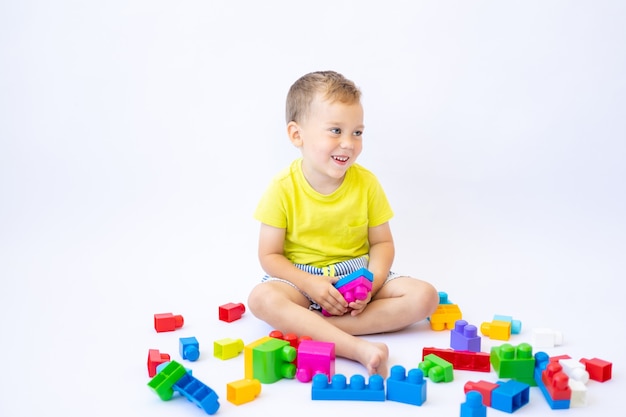 Menino fofo, criança brinca com um construtor, constrói sobre um fundo branco, isolado