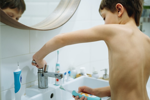 Menino fofo de 6 anos lavando escova de dente no banheiro Imagem com foco seletivo