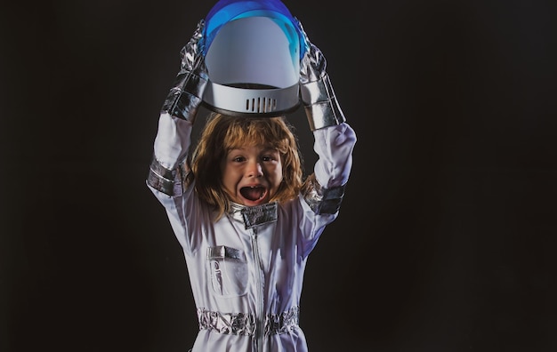 Menino fofo e animado, filho de astronauta em traje espacial segurando o capacete em fundo preto