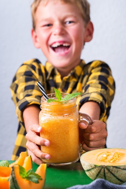 Foto menino fofo e feliz bebendo smoothie de melão saudável