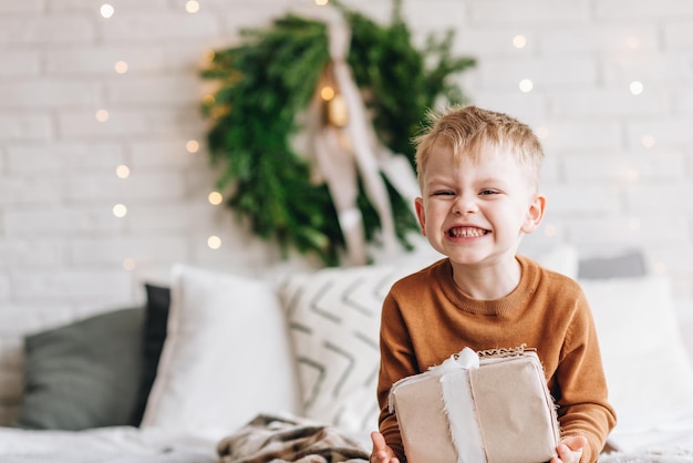 Menino fofo e feliz, caucasiano, abrindo seus presentes na manhã de Natal, árvore de Natal, grinalda, cópia spac