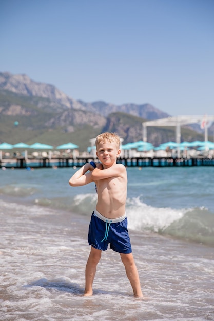 Menino fofo e sorridente com uma raquete na praia, ele está feliz. Conceito, férias de verão, descanso, diversão