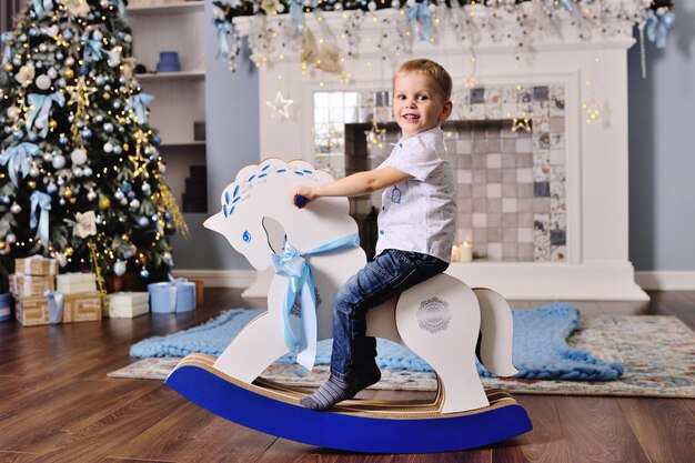 Menino fofo em um cavalo de brinquedo no contexto de uma árvore de Natal