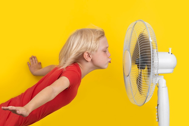 Menino fofo se refrescando com o calor na frente do ventilador