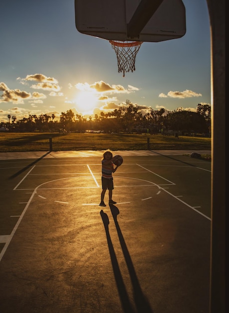 Menino fofo segurando uma bola de basquete tentando fazer um gol