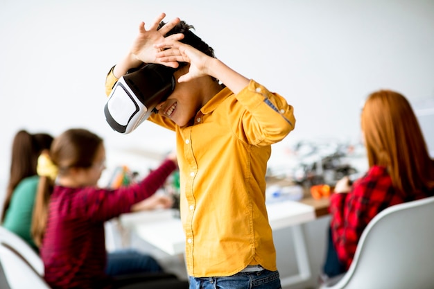 Menino fofo usando óculos de realidade virtual em uma sala de aula de robótica