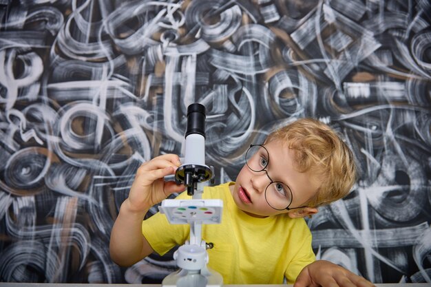 Menino gira microparafusos no microscópio em pé sobre uma mesa olhando para as lentes