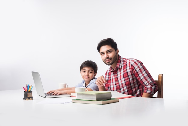 Menino indiano fofo com pai ou tutor masculino fazendo lição de casa em casa usando laptop e livros - conceito de ensino online