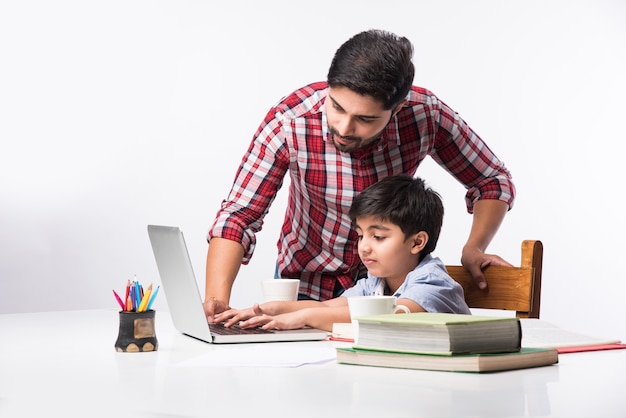 Menino indiano fofo com pai ou tutor masculino fazendo lição de casa em casa usando laptop e livros - conceito de ensino online