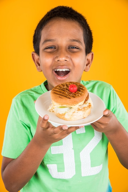 Menino indiano fofo comendo hambúrguer, pequeno menino asiático e hambúrguer, sobre fundo azul