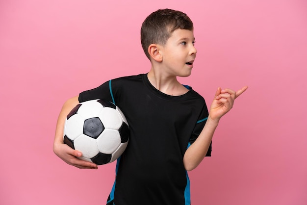 Menino jogador de futebol caucasiano isolado em fundo rosa com a intenção de perceber a solução enquanto levanta um dedo