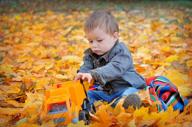 Menino jogando máquina em folhas de outono amarelas