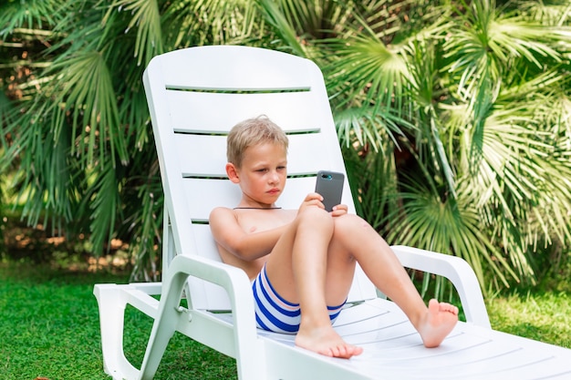 Menino jogando no telefone. Problema de transtorno de dependência de gadgets para crianças durante as férias de férias no conceito à beira-mar