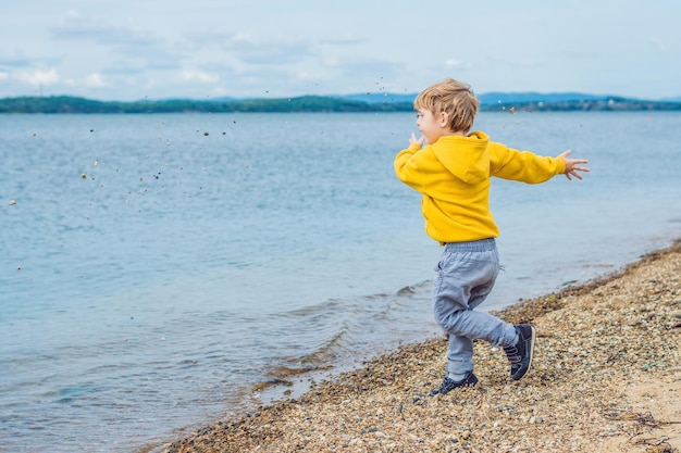 Menino jogando pedras na água do mar