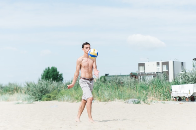 menino jogando vôlei na praia. o cara sem camisa serve a bola.