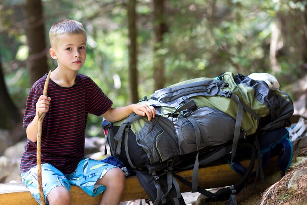 Menino jovem criança bonito com vara sentado sozinho na mochila grande turista