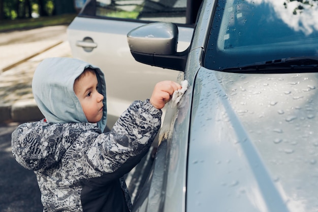 Menino lavando carro prateado Criança se divertindo e ajudando seus pais