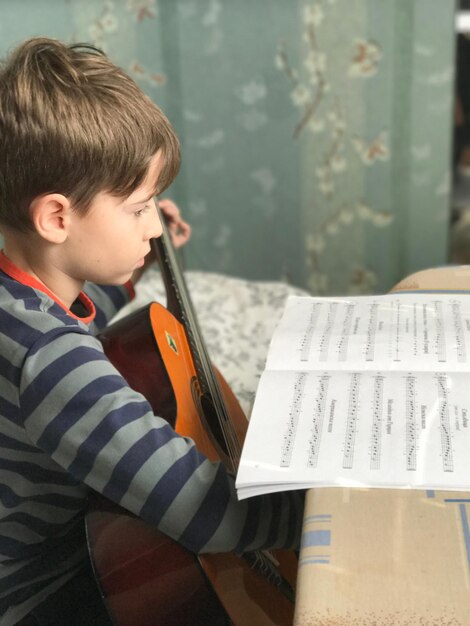 Menino lendo uma nota musical enquanto segura uma guitarra