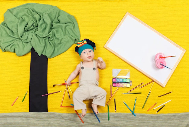 Menino lindo pintando com tintas coloridas e pincéis