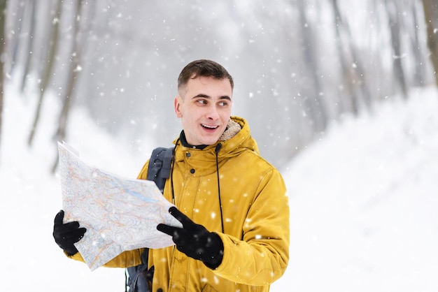 Menino loiro andando com o mapa na floresta de neve de inverno
