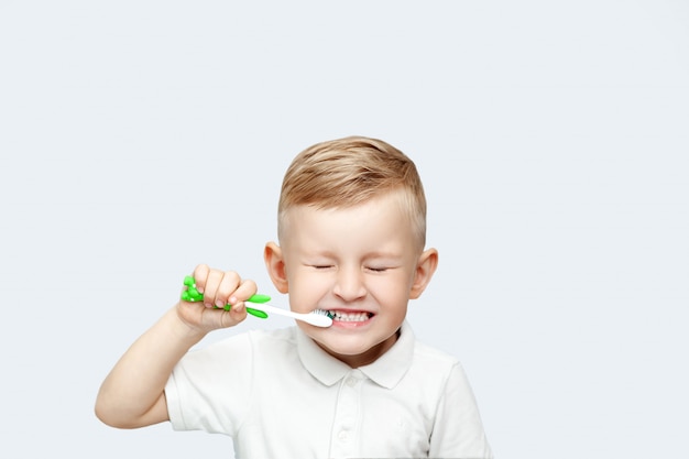 Menino loiro aprendendo a escovar os dentes no banho doméstico