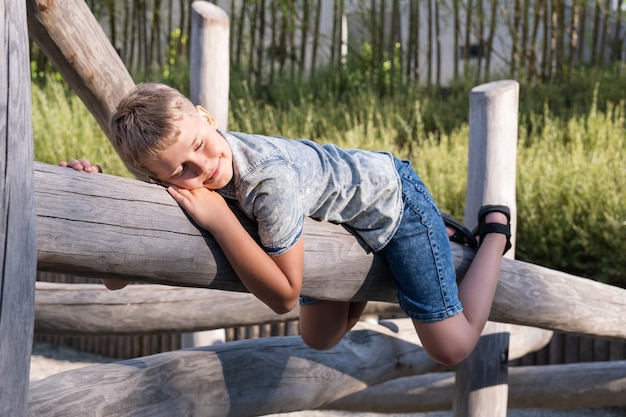 Menino loiro bonito, o menino encontra-se em uma viga de madeira no playground em um parque público.