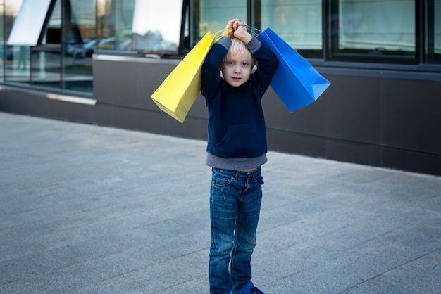 Menino loiro cansado com sacolas de compras.