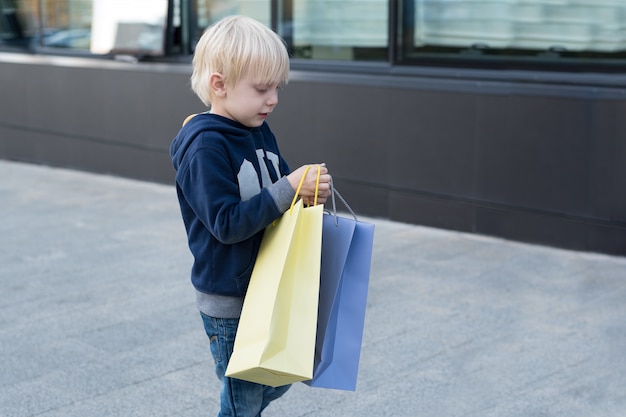 Menino loiro com sacolas de compras, família de compras